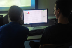 Zwei Teilnehmende schauen auf einen Bildschirm wo eine karierte Anzeige mit einem gelben und einem roten Dreieck zu sehen ist.