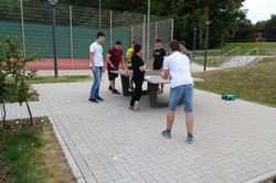 do-camp-ing Teilnehmerinnen und Teilnehmer spielen zusammen Tischtennis.