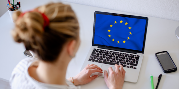 Auf dem Bild ist eine Studentin am Laptop zu sehen, dessen Bildschirm die Europaflagge zeigt.