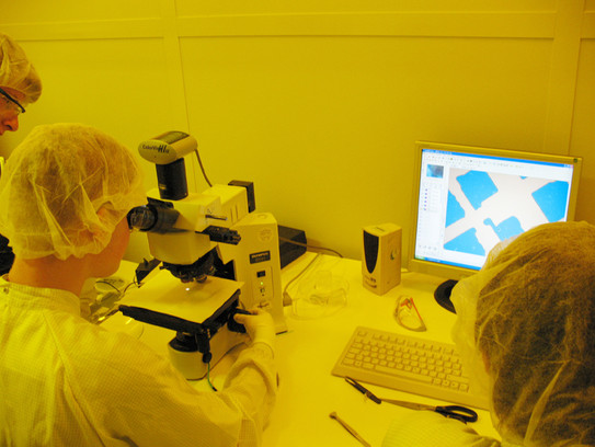 Die Teilnehmenden schauen sich im Reinraum eine Probe durch ein Mikroskop an