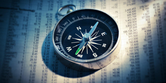 Nahaufnahme eines Kompass, der auf einem Blatt mit einer Zahlen-Tabelle liegt