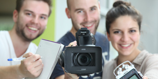 Two young men and a young woman with notepad, video camera and audio recorder
