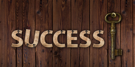 Wooden letters "Success" on a wooden base, next to it an ancient key