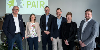 Das Bild zeigt mehrere Personen vor einer Leinwand mit der Aufschrift "Agile PAIR".