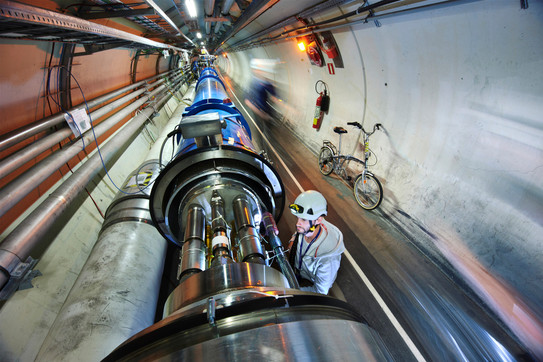 A man wearing a helmet stands in front of a long tube in a tubular long tunnel.