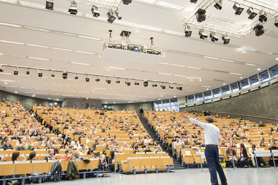 Ein Mann steht vor einem großem Publikum in einem Hörsaal.