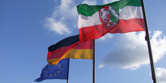 Es ist eine NRW-Flagge, eine Deutschlandflagge und eine EU-Flagge zu sehen.