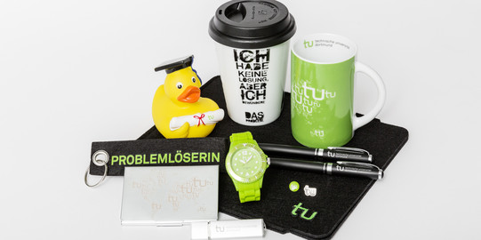 Various TU Dortmund merchandise, including a mug, a watch and a keychain, lie on a table