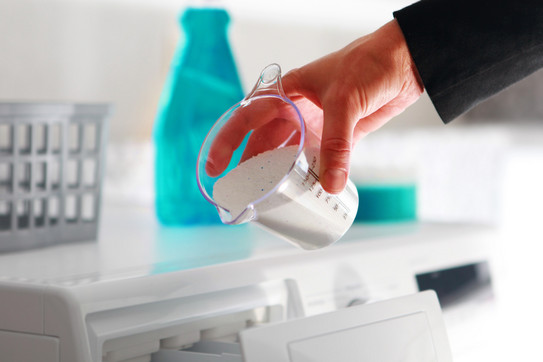 Das Foto zeigt eine Hand, die Waschpulver in eine Waschmaschine gibt.