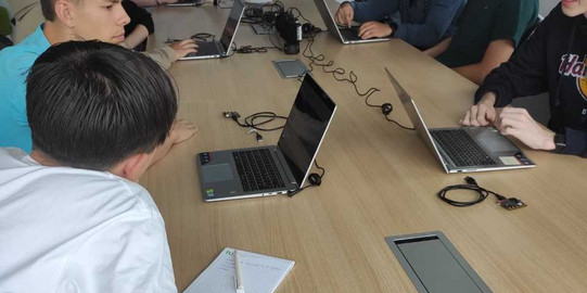 Schüler*innen sitzen am Gruppentisch und arbeiten an Laptops