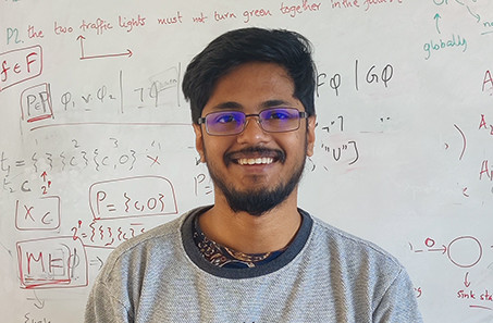 A photo of doctoral student Rajarshi Roy in front of a white board. A smiling man in a sweater.
