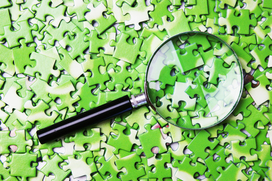 A magnifying glass on a pile of light green jigsaw puzzle pieces.