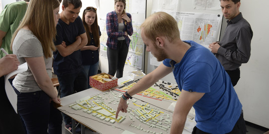 Eine Gruppe von Studenten stehen um einen Tisch mit einem Modell für die Stadtplanung.