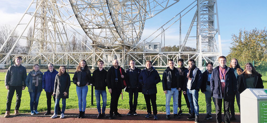 A group of young people pose for a group photo in front of a structure made of white metal.