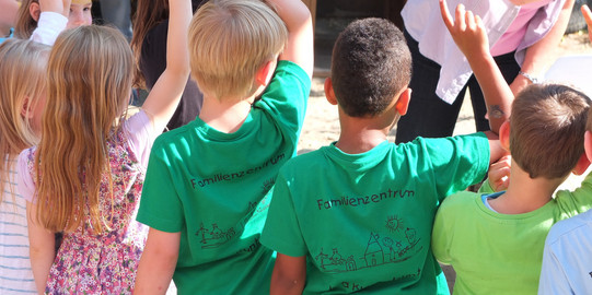 Eine Gruppe von Kindern mit grünen T-Shirts sind von hinten zu sehen und melden sich.