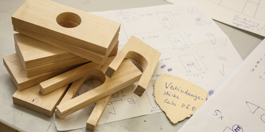 Einzelne Bausteine eines Holzmodells liegen gestapelt aufeinander.