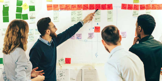 Veranstaltungen Gruppe Studierender vor einem Whiteboard mit farbigen Post-Its