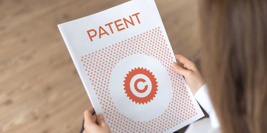 Schutzrechte Frau hält weißes Papier mit der roten Aufschrift Patent in der Hand