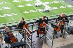 Ein Streichquartett spielt Musik, im Hintergrund ist das Fußballfeld zu sehen