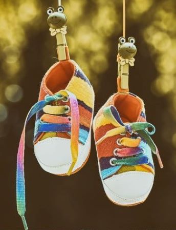 Small children's shoes in rainbow colors hang on a line.