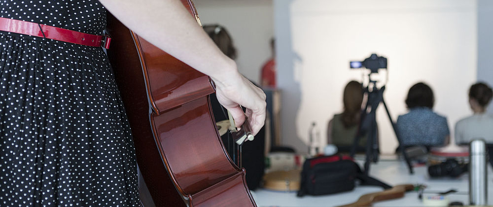 Nahaufnahme des Bogens einer Cellistin im Hintergrund sitzen Menschen