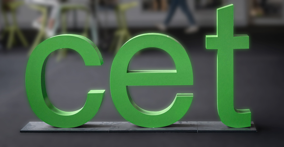 Three green letters c e t stand in a room