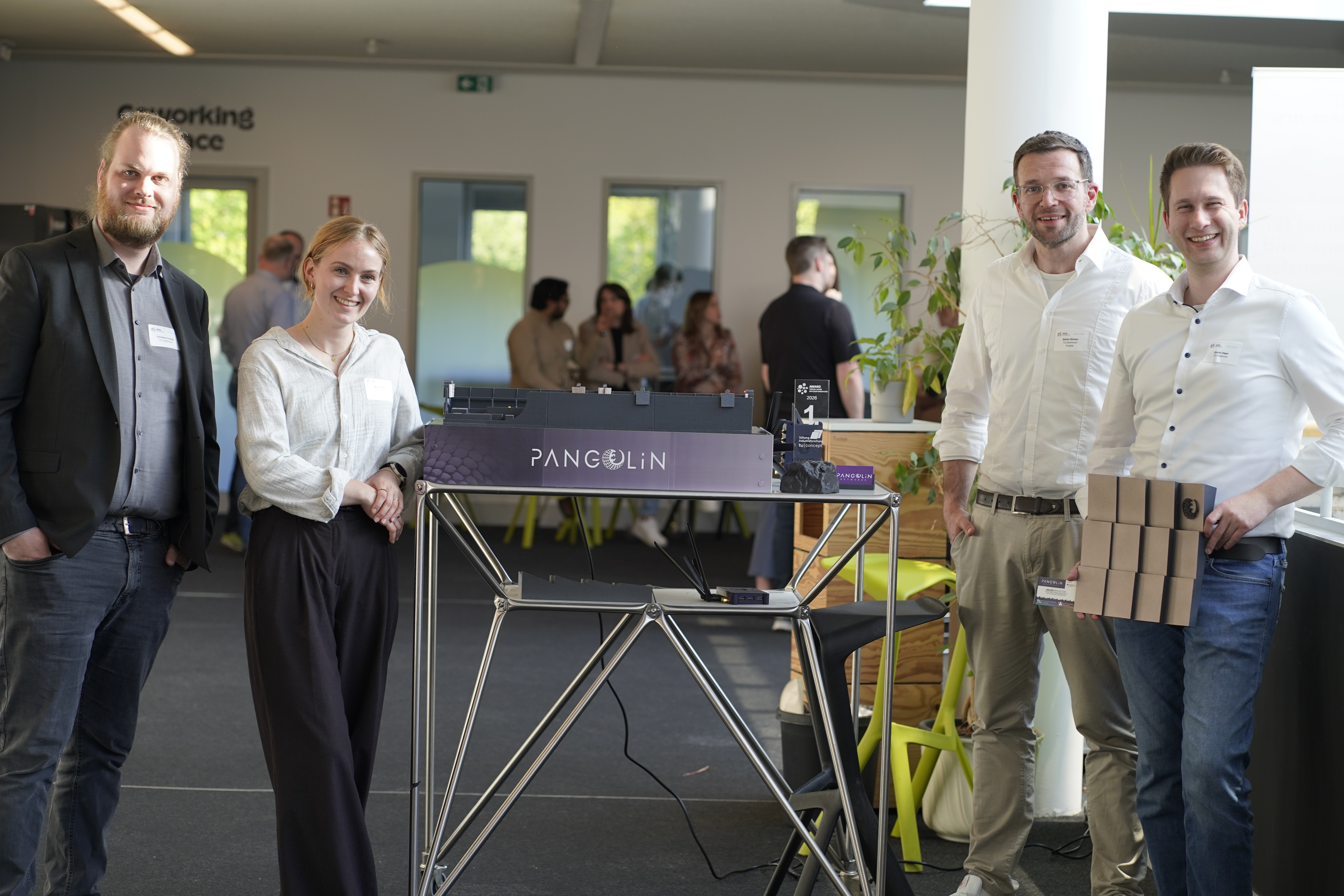 Foto: Vier Personen stehen neben einem Tisch mit einem ausgestellten Modell bei einer Veranstaltung.