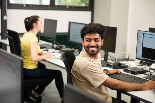 Foto von zwei Studierenden die an PCs arbeiten