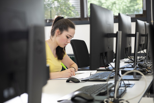 Foto einer jungen Frau vor einer Reihe an Computerbildschirmen