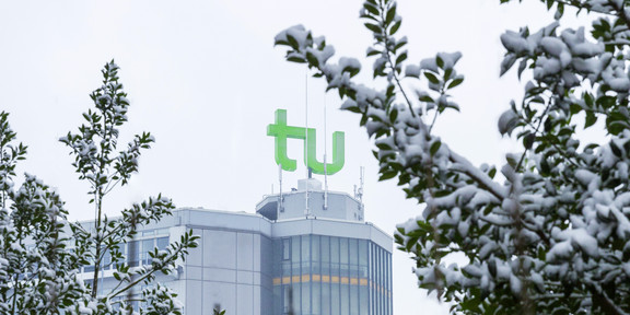 Mathetower im Schnee Im Vordergrund schneebedeckte Zweige, im Hintergrund der Mathetower mit grünem TU-Logo auf dem Dach