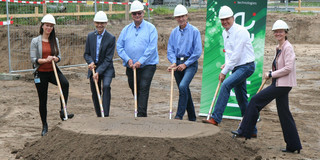 Six people are standing with spades in their hands behind a small pile of heaped up earth.