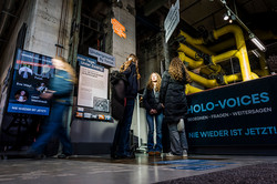 Foto: Mehrere Personen betrachten Ausstellungstafeln in einem industriellen Raum.