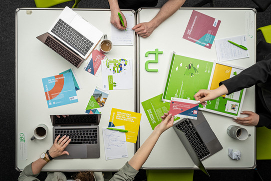 View of a meeting table from above, several people are sitting at the table, laptops and TU materials are spread out