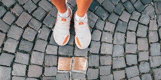 Vogelperspektive von zwei Stolpersteinen und zwei Paar Beinen