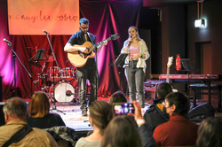 Tag der offenen Tür Band Eine Frau singt und ein Mann spielt Gitarre und beide stehen auf einer kleinen Bühne vor Publikum.