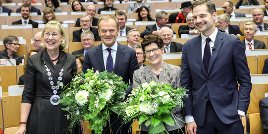 Zwei Frauen und zwei Männer in festlicher Kleidung stehen nebeneinander und lächeln