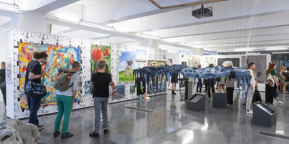 Rundgang Kunst Überblick In einem Ausstellungsraum stehen und Hängen verschiedene Gemälde, Fotografien und Plastiken.
