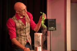 A man in a red shirt and patterned vest conducts an experiment.