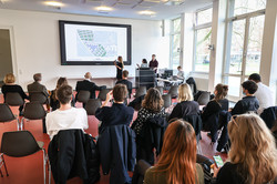 Eine Gruppe von Frauen und Männern sitzen vor einer Leinwand und hören einer Präsentation zu.