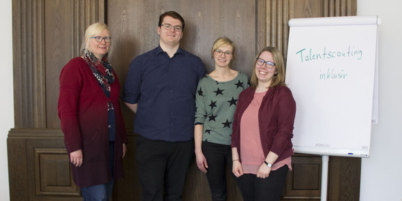 Three women and one man are standing next to a flipchart.