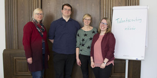 Drei Frauen und ein Mann stehen neben einem Flipchart.