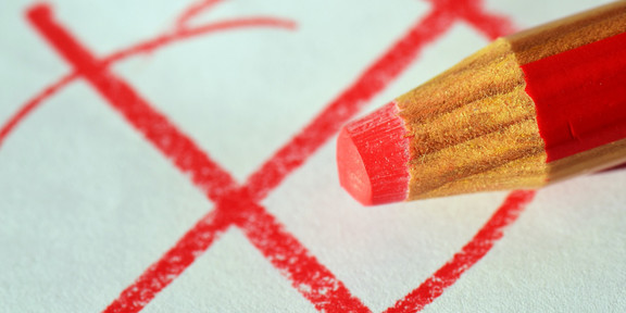 A red cross in a red circle. In the foreground a red crayon.