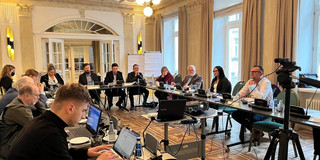 A group of people sit at tables and work on laptops.