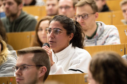 A woman in the audience holds a microphone and asks a question.