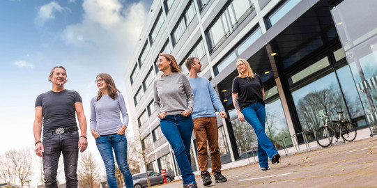 Gruppe von Beschäftigten geht an einem modernen Gebäude entlang.
