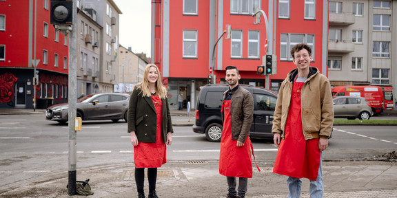 A woman and two men are standing in front of an intersection.