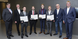 EIn Foto von acht Männern in Anzügen, vier von ihnen halten Urkunden in der Hand.