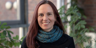 Portrait image of a woman in front of a window, this woman is Kerstin Guhlemann.