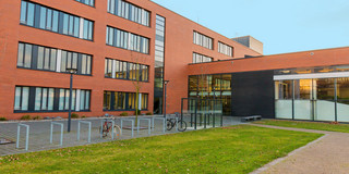 Ein vierstöckiges rotes Klinkergebäude mit Fahrradständern vor dem Eingang.