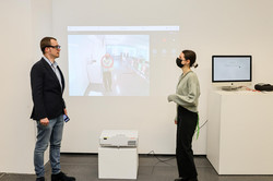 Ein Mann und eine Frau mit Maske unterhalten sich in einem Ausstellungsraum